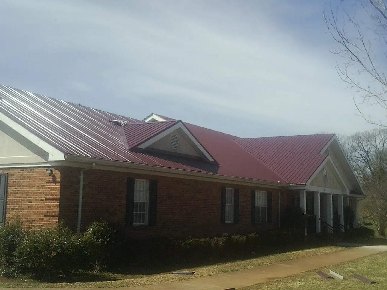 Red metal roof with gabled entries on a long brick building, from a Hail Damage Roof Repair job in Grants Pass