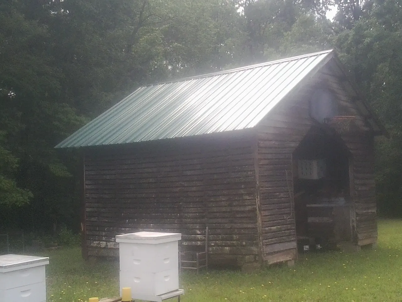 Green metal roof on a weathered barn beside stacked beehives in Grants Pass