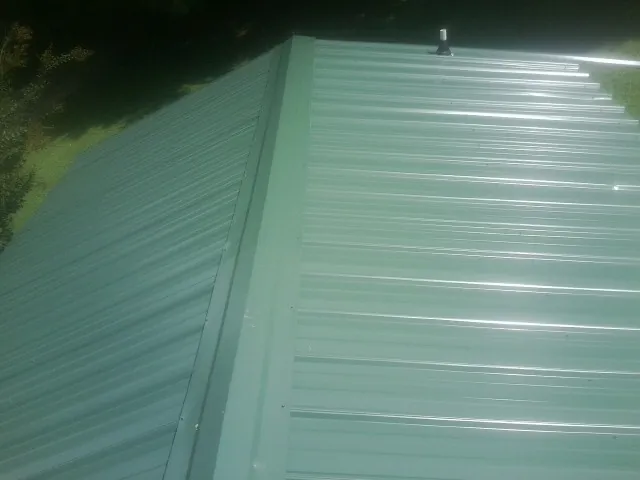 New green metal panels meeting at the ridge of a roof — Flat Roof Repair work by our crew in Grants Pass