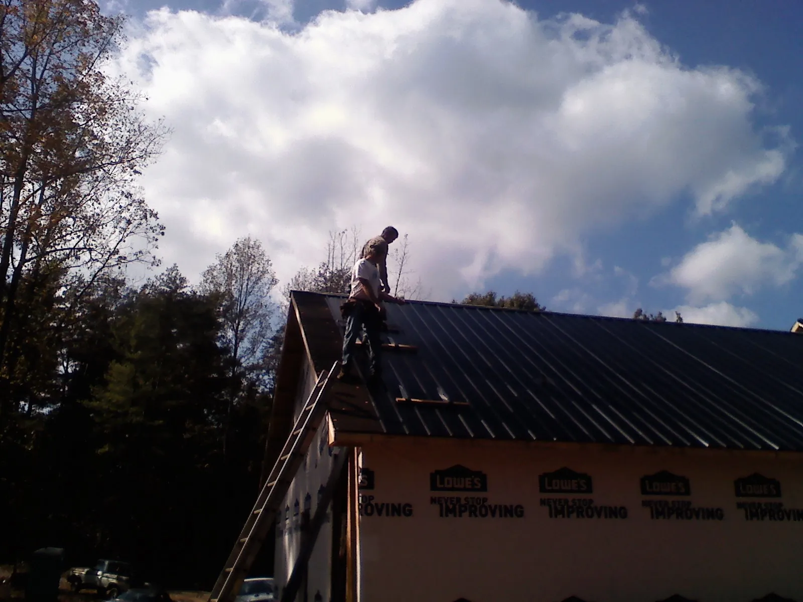 Roofer fastening dark metal panels high against a cloudy sky, from a Roof Inspection job in Grants Pass