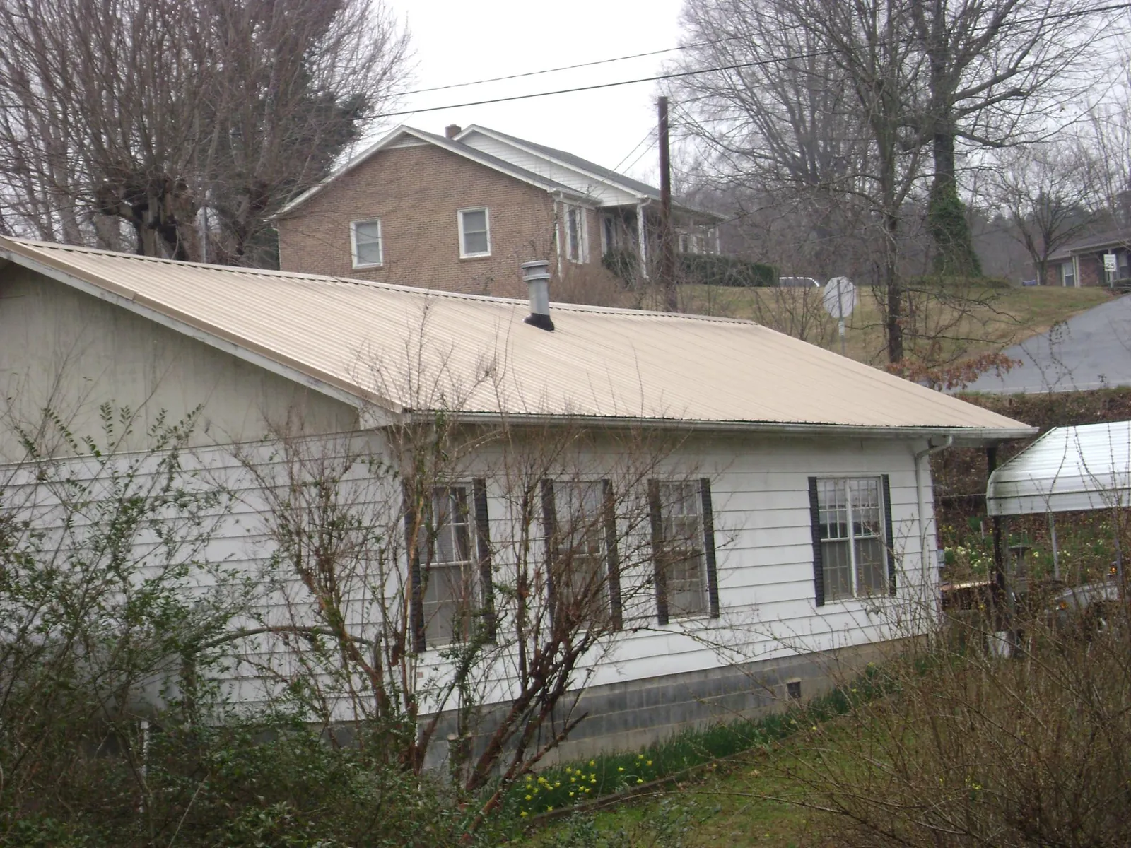 Tan metal roof on a white sided house set into a hillside — Commercial Roofing by Roofing Brothers in Grants Pass